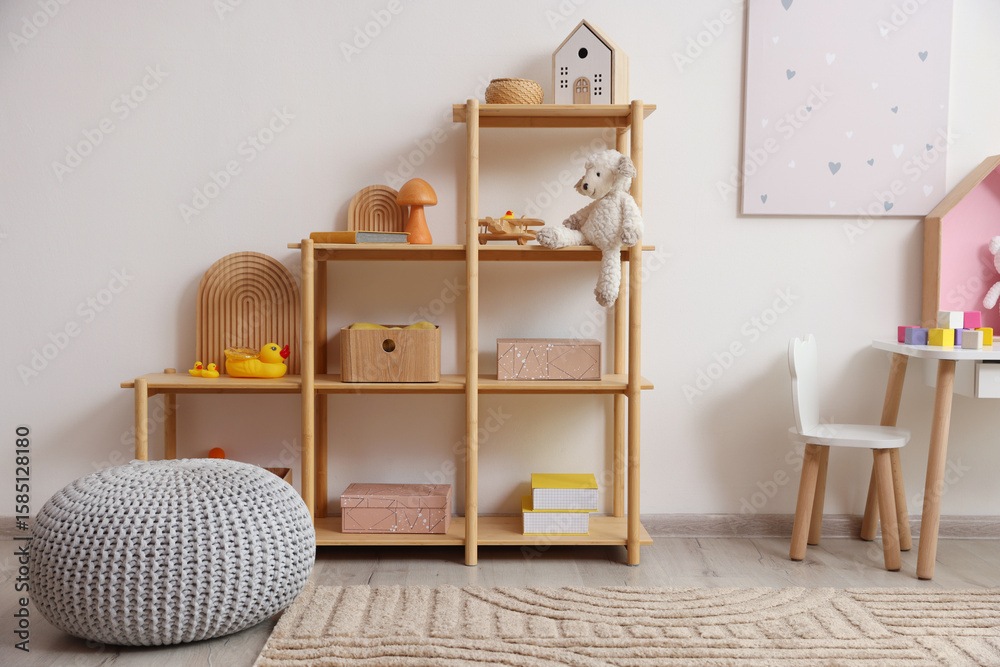 Obraz premium Shelving unit with decor, toys and pouf in stylish playroom. Interior design