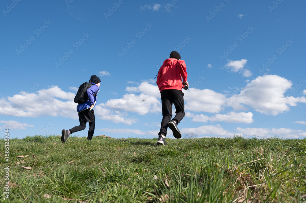 Two boys run across a grassy hill under a bright blue sky, enjoying a sunny day outdoors. Two boys run across a grassy hill under a bright blue sky, enjoying a sunny day outdoors.