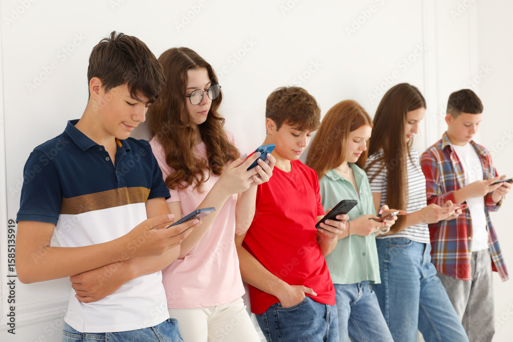 Teenagers with smartphones near white wall indoors Teenagers with smartphones near white wall indoors
