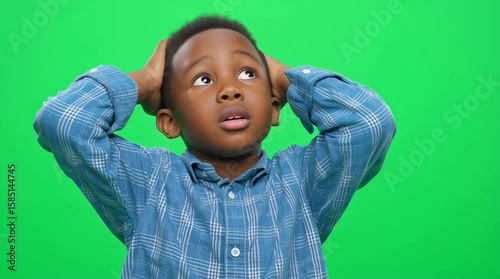 An african american kid looking up with hands on head against a green screen background. Boy expressing confusion, upset.