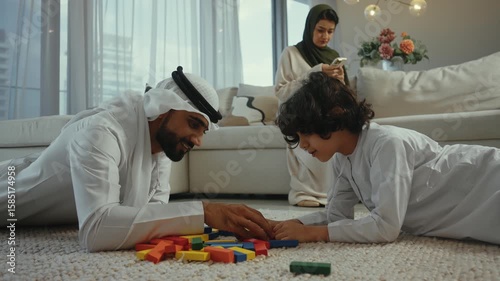 Loving muslim parents engaging with young son while building colorful block tower together on living room carpet, showcasing family bonding and playful learning moment