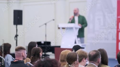 Professional presentation with male speaker on stage and audience attending in a conference venue.