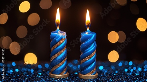 Two blue candles with gold swirls, burning brightly against a dark background with bokeh lights