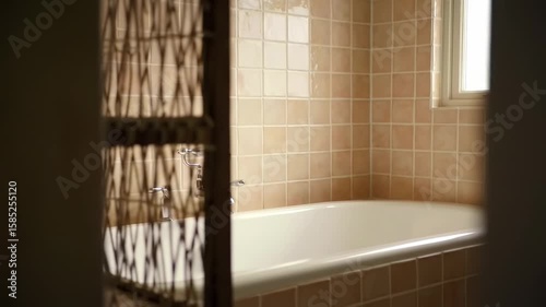 Beige tiled bathroom with a woven screen and a white bathtub