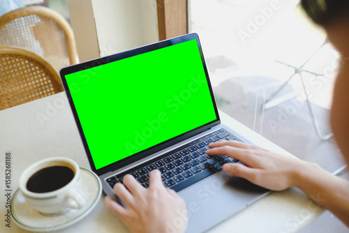 Fotografie A person working on a laptop with a blank green screen in a cafe by the window