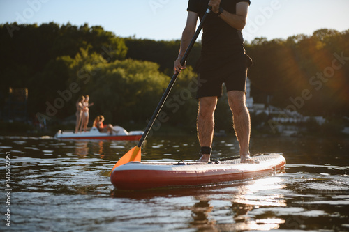 Photos Sportsman paddling on sup board at sunset on lake with pedal boat in background