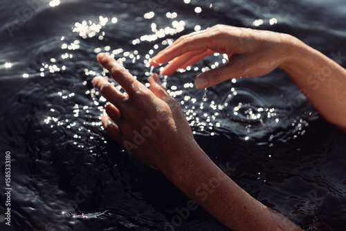 Sunlight reflects off the surface of water as hands gracefully move through, creating ripples. tranquil setting invites relaxation and connection with nature