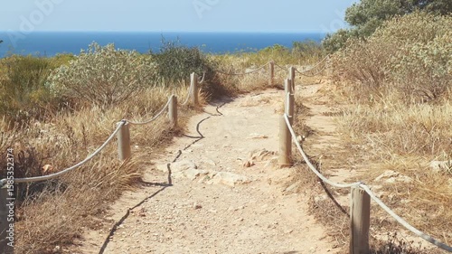 Tourist walking path on Cape Sant Antoni near Xabia, Spain, bordered by rope and wooden posts, overlooking the Mediterranean coastline under a clear blue sky