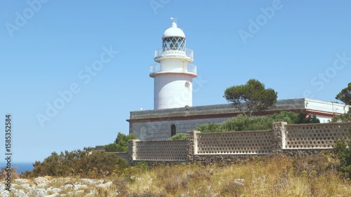 Scenic view of the white lighthouse at Cape Sant Antoni near Xabia, Spain, standing on a cliff above the Mediterranean Sea under a clear blue sky