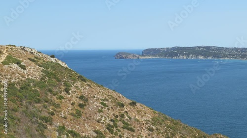 Wide scenic view of the Mediterranean Sea from the cliffside viewpoint at Cape Sant Antoni in Spain, with clear blue water and sky stretching to the horizon