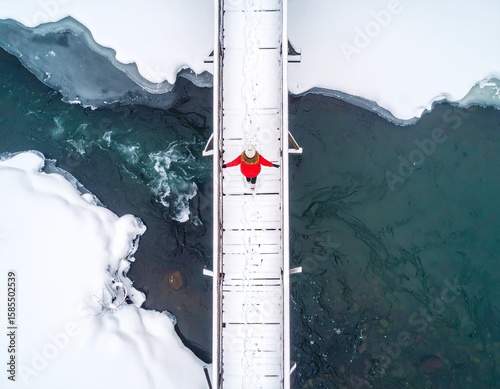 Aerial view of a person on a snowy bridge over a frozen river