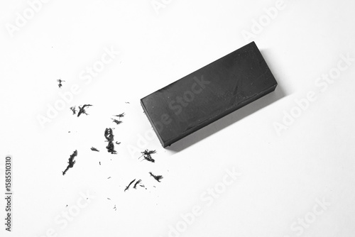 A black eraser sits on a white surface, surrounded by eraser shavings.