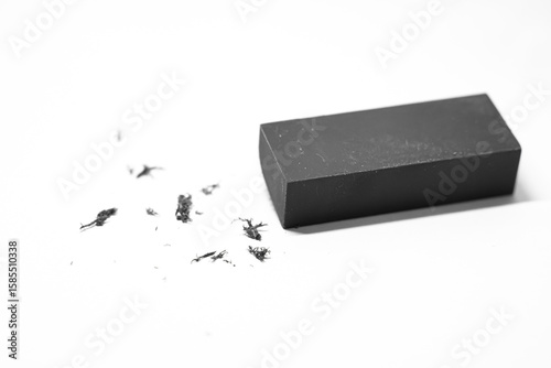 A dark gray rectangular eraser rests on a white background, surrounded by small graphite shavings.