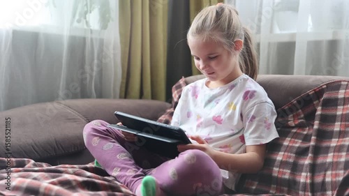 child girl uses a tablet sitting on the couch at home. Generation Z. gadget addiction. 