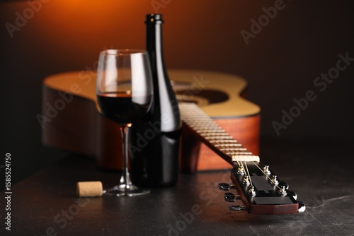 Fotografía Acoustic guitar and red wine on black table with brown light, closeup