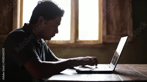 Silhouette of a man working from home typing on a laptop computer in a dimly lit room