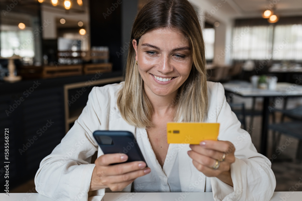 Happy businesswoman holding credit card doing online shopping through smart phone at restaurant Happy businesswoman holding credit card doing online shopping through smart phone at restaurant