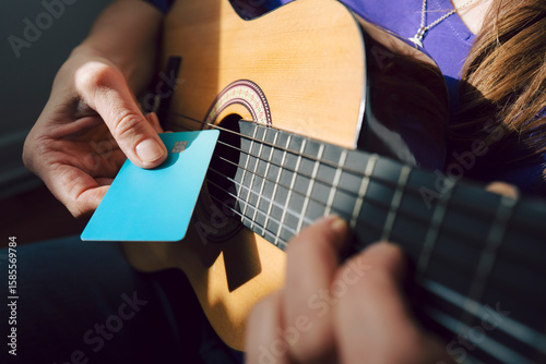 Person using a credit card to play an acoustic guitar at home in sunlight