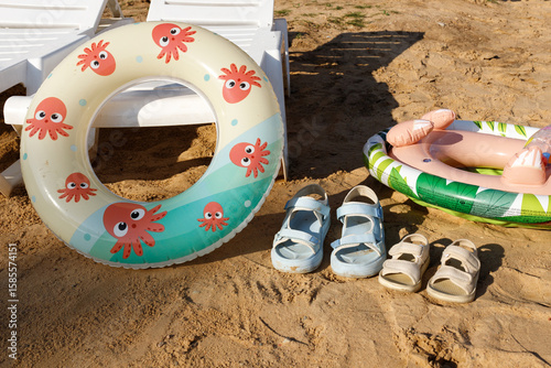 Several white sun loungers, inflatable swimming rings, children's sandals stand on the sand on the beach on a sunny evening. No one uses