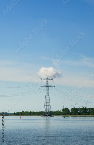 Power pylon and cloud over water with wind turbines in the Netherlands