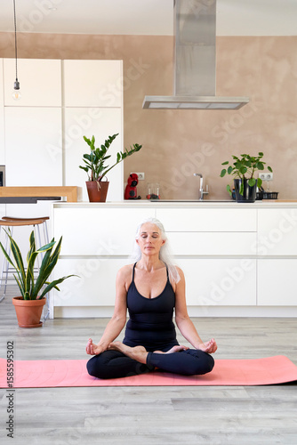 Mature woman with eyes closed sitting in lotus position at home