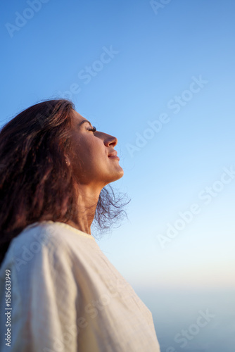 Young woman breathing fresh air and enjoying freedom under blue sky, mindfulness and wellbeing concept