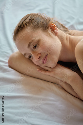 Fotografie Freckled woman lying peacefully with dreamy smile on bed in natural daylight