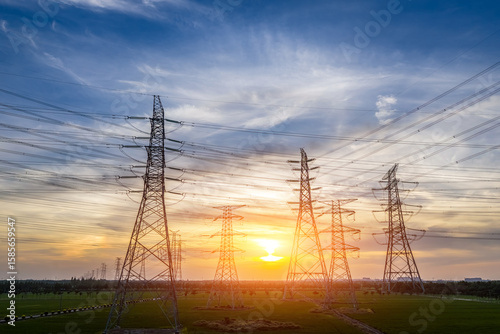 High voltage power tower and transmission lines silhouetted against beautiful sunset sky in a rural field