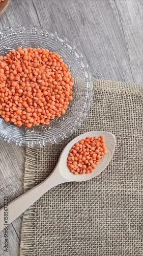 Dried red lentils in a decorative glass plate and wooden spoons on a gray background