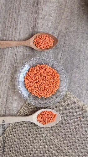 Dried red lentils in a decorative glass plate and wooden spoons on a gray background