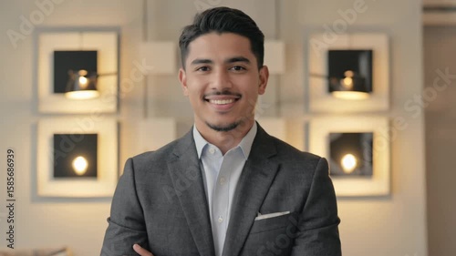 Professional, young Latino man in business attire smiling for a portrait. He is wearing a suit and tie and has a modern urban office background.