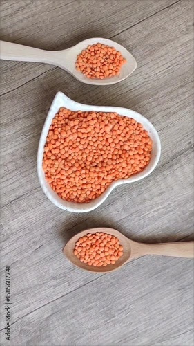 Dried red lentils in a decorative glass plate and wooden spoons on a gray background