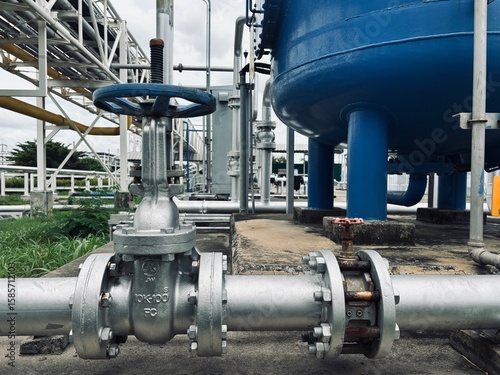 oil tank in the factory. Industrial valve connected to a large storage tank with stainless steel piping in a factory setting. Commonly used in chemical plants, refineries, or water treatment systems.