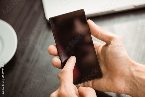 Hands are holding smartphone in flat design dark wood tabletop close-up, with laptop and plate