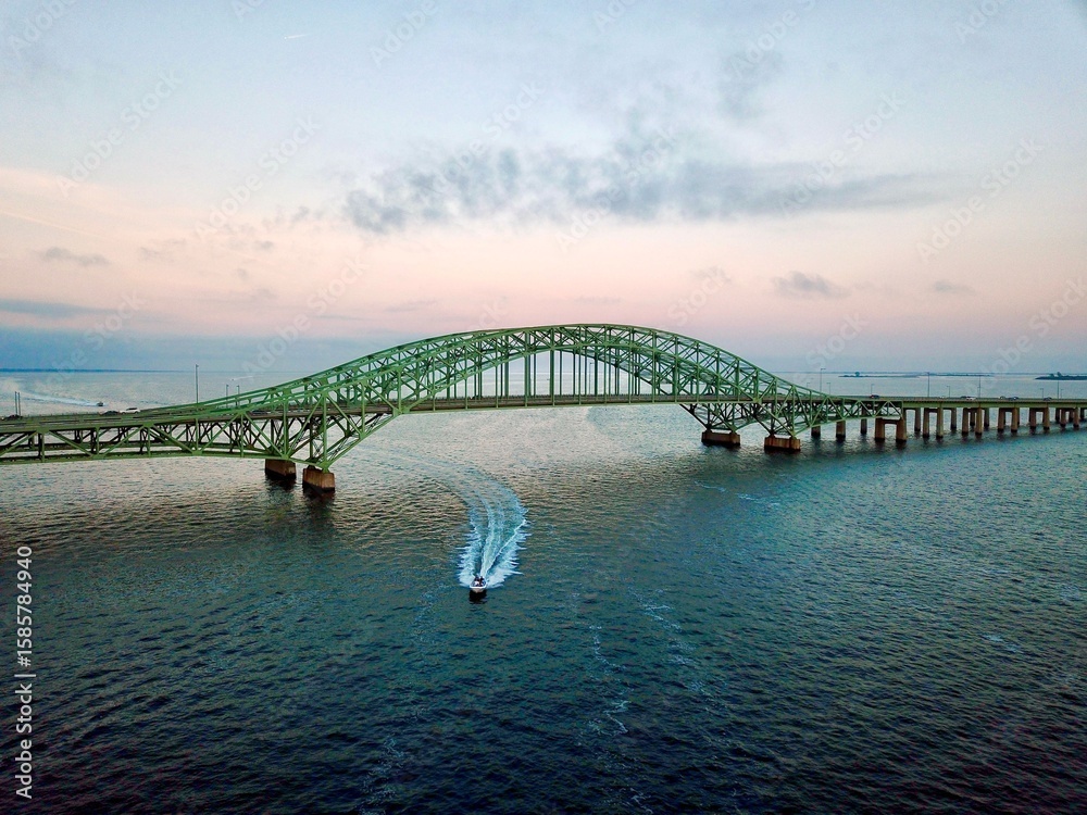 Obraz premium Aerial view of a boat under a bridge at sunset.