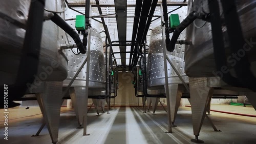 Steel cisterns for wine production processes, metal tanks with black pipes and technical regulators on winemaking factory, viticulture concept