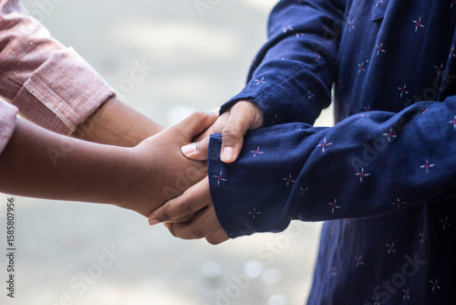 A young man using both hands to shake hands with a man wearing a Punjabi.