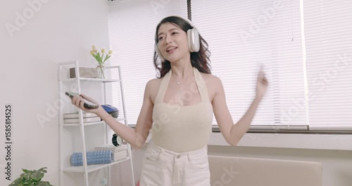 Asian woman wearing headphones  listen music singing and dancing happily in living room. Leisure activity, Lifestyle.
