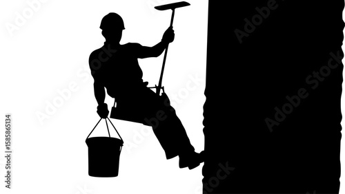 Silhouette of window cleaner holding squeegee and bucket while suspended on building, cleaning glass pane