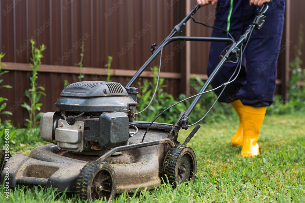 Fototapeta premium A lawn mower man mows the grass in the backyard. Agricultural machinery for garden maintenance. The concept of gardening and country life. The banner.
