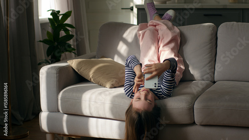 Little girl child lying on sofa using mobile phone smartphone gadget technology online meeting communication gesticulating conversation talk video call chat daughter kid home internet network virtual