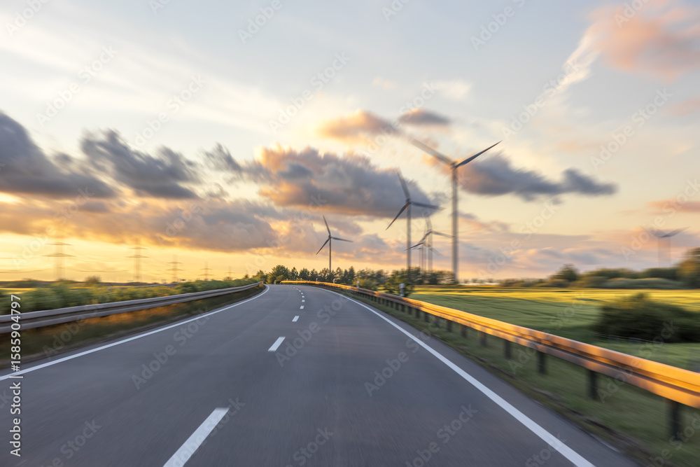 Fototapeta premium Wind farm along the road. Nature energy at sunset. Motion and technology