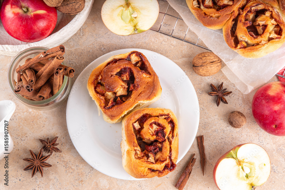 Fototapeta premium Apple cinnamon roll, sweet cinnabon buns with apple filling. Viral apple pie rolled buns, on beige table with cinnamon sticks, apples, nuts and spices