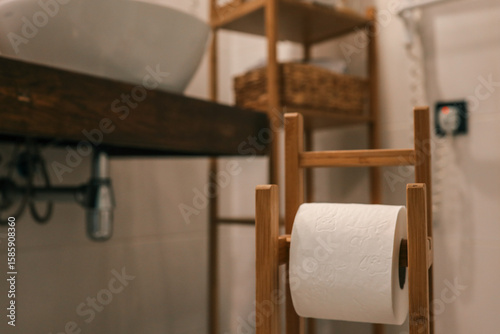 Stylish modern bathroom with wooden toilet paper holder, white ceramic toilet, towel rack, sink, and wicker storage basket. Clean, minimalistic, and well-organized space