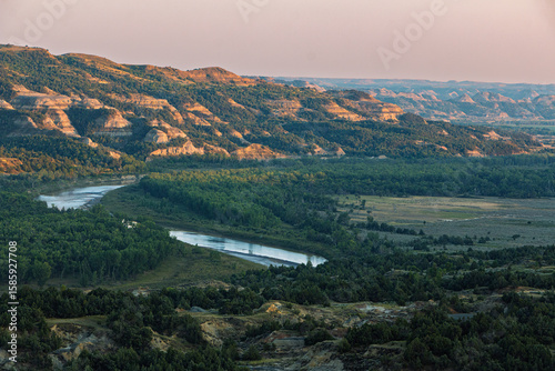 Sunset over the badlands and Little Missouri River with colorful mountains, sky, and green valley. Theodore Roosevelt National Park, North Unit, North Dakota, USA
