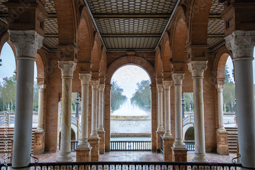 A majestic view through the arched gallery of Plaza de Espana in Seville Spain, showcasing the central fountain and surrounding architectural beauty.