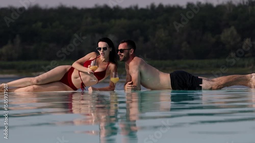 Young beautiful couple relaxing and enjoying vacation in the pool. Concept love, summer leisure, luxury, romance and tropical lifestyle.