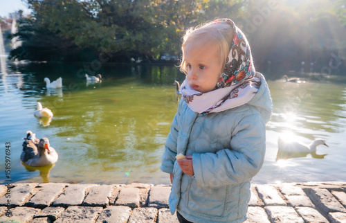 A little girl is standing by a pond with ducks