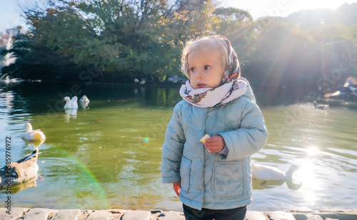 A little girl is standing by a pond with ducks