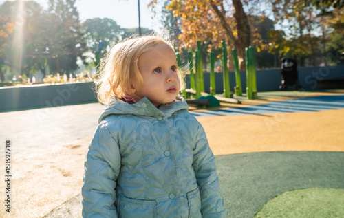 A little girl wearing a blue coat stands in a park
